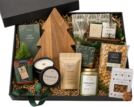 Black box holding a tree-shaped wooden board, hot cocoa, a Fraser fir candle, glazed pecans, caramel popcorn, gingerbread cookies and a small potted evergreen