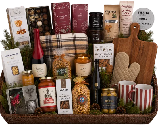 Large woven tray holding a plaid blanket, red wine, olive oil, chocolates, two striped mugs, a cutting board, pasta, sauce, pecans, popcorn and gingerbread cookies